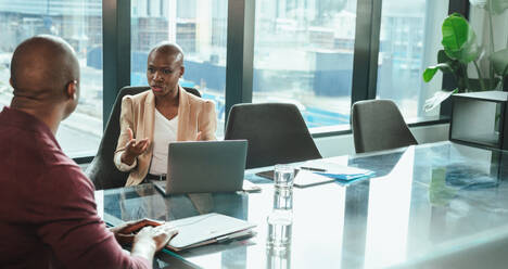 Two professionals, a black mature woman and a colleague, collaborate and discuss a project in an office. They work together on a computer, showcasing teamwork and productivity. - JLPSF31370