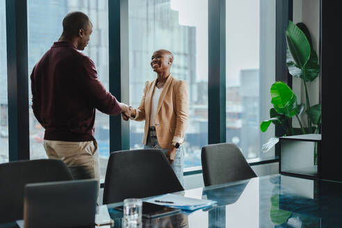 Two business people, a man and a woman, have a successful meeting in a corporate boardroom. They shake hands, symbolizing partnership, collaboration, teamwork and success. - JLPSF31372