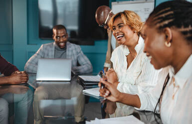 Eine Gruppe von Fachleuten in einem Büro hat ein erfolgreiches Geschäftstreffen. Sie diskutieren, lachen und zeigen eine fröhliche Atmosphäre der Teamarbeit im Sitzungssaal. - JLPSF31389