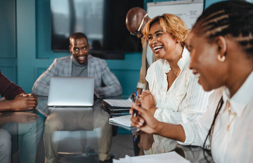 Group of professionals in an office have a successful business meeting. They discuss, laugh, and display a happy teamwork atmosphere in the boardroom. - JLPSF31389