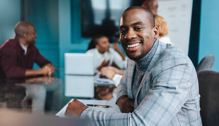 Professional businessman in a stylish suit is showcasing confidence with a warm smile during a collaborative team meeting in a contemporary office setting, embodying leadership and positivity. - JLPSF31390