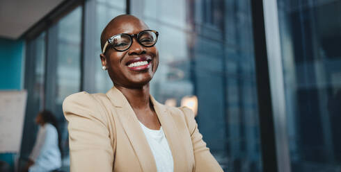 Businesswoman in a boardroom meeting. She looks happy and successful, wearing glasses and standing in a panoramic office. Her professional smile exudes confidence and success in the workplace. - JLPSF31405