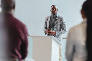 Professional businessman with a warm smile engages an audience during a corporate presentation. Audience interaction and effective communication in a business setting are captured in this image. - JLPSF31408