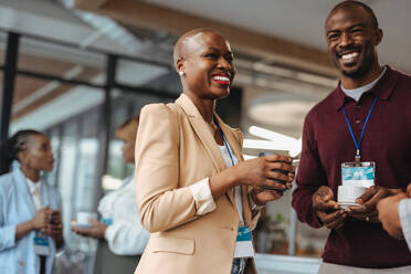Successful business people networking while enjoying a casual coffee break at a conference. They are exchanging ideas with warm, genuine smiles, promoting a positive work culture and collaboration. - JLPSF31441