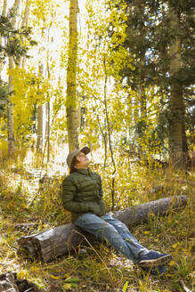USA, New Mexico, Pensive boy sitting on log in Santa Fe National Forest - TETF02575