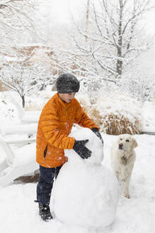 Boy with his dog building snowman - TETF02579