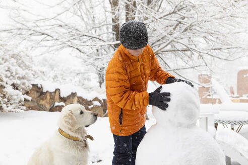 Boy with his dog building snowman - TETF02580