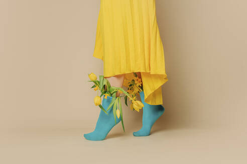 Woman wearing yellow skirt with tulips in blue socks against beige background - VSNF01694