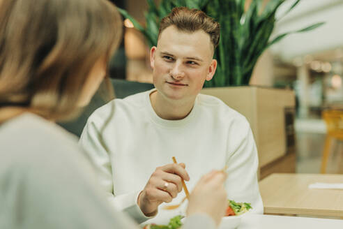 Young man eating salad with girlfriend at mall - VSNF01695