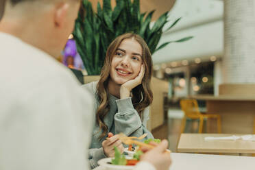 Smiling woman leaning on elbow and having salad with boyfriend at mall - VSNF01696