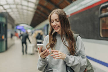 Smiling young woman using smart phone at train station - VSNF01704