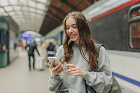 Smiling young woman using smart phone at train station - VSNF01704
