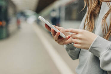 Woman surfing net through smart phone at station - VSNF01705