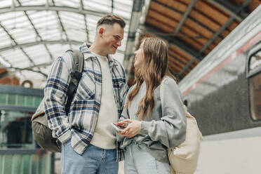 Young couple with backpacks standing at railroad station - VSNF01706