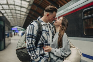 Loving couple standing with backpacks at railroad station - VSNF01707