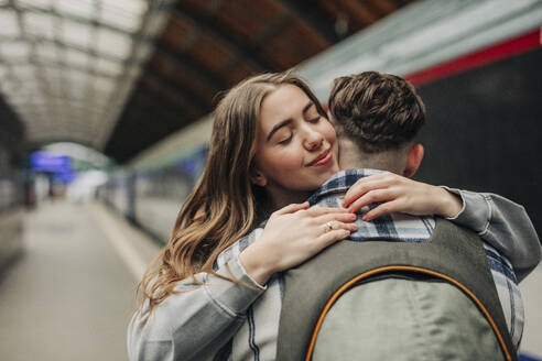 Smiling woman embracing boyfriend at station - VSNF01708