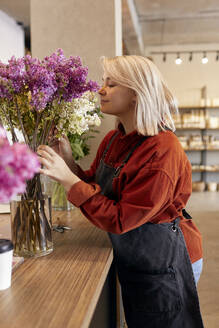 Smiling florist smelling flowers at store - SANF00203