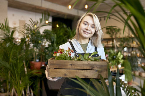 Happy gardener holding crate of plants in garden center - SANF00216