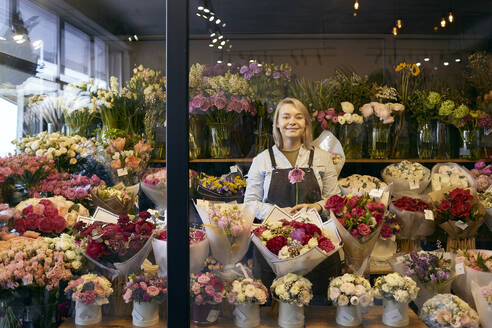 Smiling florist standing amidst bouquet of various flowers at shop - SANF00219