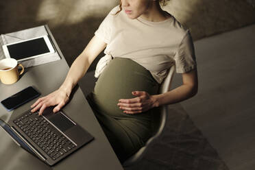 Schwangere Freiberuflerin mit Laptop am Schreibtisch im Heimbüro - DSHF01615