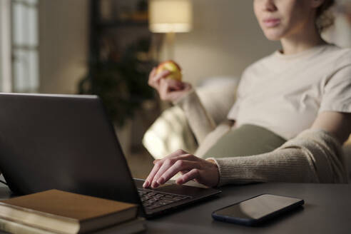 Werdende Mutter, die einen Apfel hat und einen Laptop im Heimbüro benutzt - DSHF01627