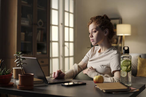 Junge schwangere Freiberuflerin arbeitet am Laptop im Home Office - DSHF01628