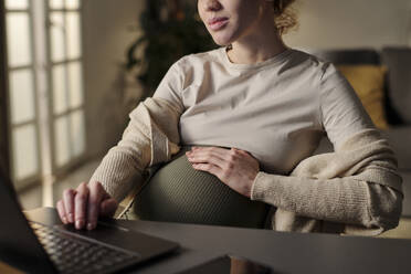 Young pregnant businesswoman working on laptop from home - DSHF01629