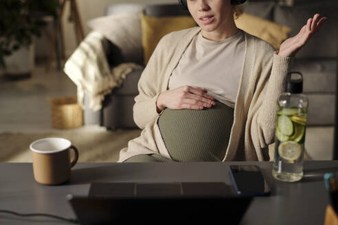 Schwangere Freiberuflerin bei Videogespräch über Laptop im Home Office - DSHF01631