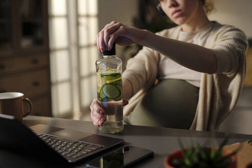 Werdende Mutter öffnet Flasche mit frischem Zitronen-Gurken-Getränk - DSHF01633