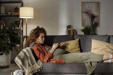 Young expecting mother using smart phone on sofa in living room - DSHF01637