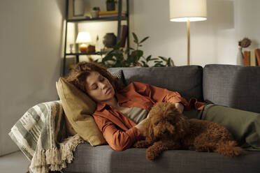 Müde schwangere Frau, die sich mit ihrem Hund zu Hause auf dem Sofa ausruht - DSHF01643