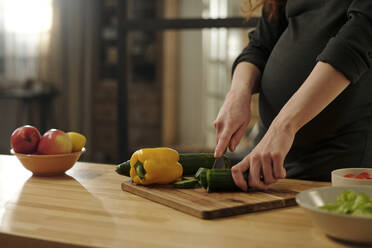 Schwangere Frau schneidet Gemüse in der Küche - DSHF01662