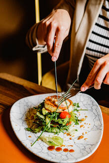 Person, die eine Zange benutzt, um ein raffiniertes gegrilltes Gericht mit frischem Salat auf einem marmorierten Teller zu servieren - ADSF53209