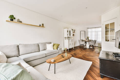 Geräumiges Wohnzimmer mit grauem Sofa und Holzboden, das nahtlos in einen Essbereich mit Tageslicht übergeht. - ADSF53281