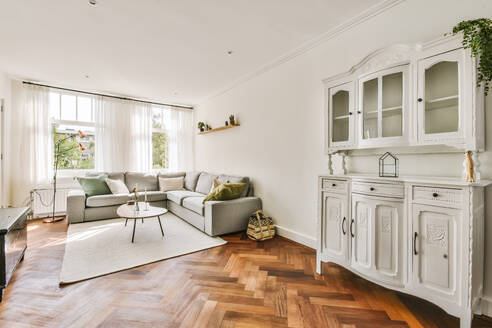 Ein modernes Wohnzimmer mit einem Sektionssofa, einem schicken Couchtisch und einem klassischen weißen Schrank, mit Parkettboden und transparenten Vorhängen. - ADSF53282
