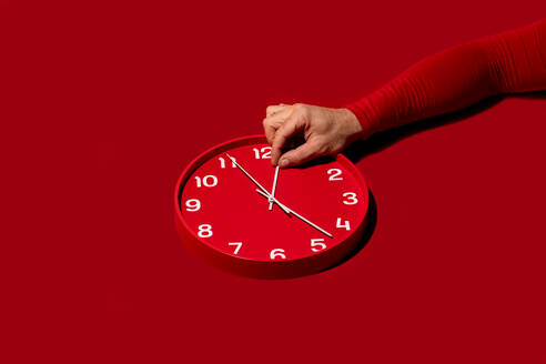 A hand moving the minute hand of a modern red wall clock set against a matching red background - ADSF53327