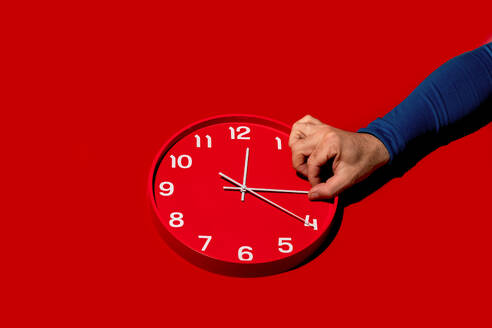 Der Zeiger einer Person stellt die Zeit auf einer roten Wanduhr mit auffallend rotem Hintergrund ein und veranschaulicht so das Zeitmanagement - ADSF53328