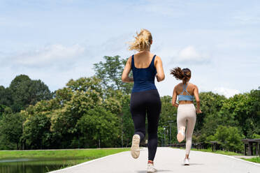 Full body of anonymous young women in activewear and sneakers jogging on road during cardio workout near bushes in Thailand Chiang Mai - ADSF53332