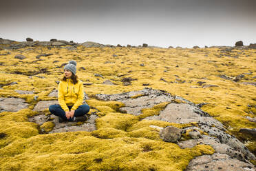 Schöne junge Frau, die auf einem Felsen sitzt und von isländischem Moos umgeben ist - INGF12878