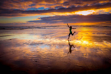 Silhouette einer Frau, die bei Sonnenuntergang an den Strand springt - INGF12889