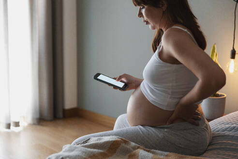 Schmerzhafte schwangere junge Frau zu Hause, die per Telefon medizinische Hilfe anfordert - INGF12905