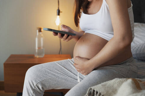 Schmerzhafte schwangere junge Frau zu Hause, die per Telefon medizinische Hilfe anfordert - INGF12906