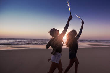 Teenage friends running on a beach with fireworks - INGF12919