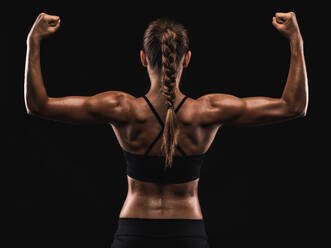 Studioaufnahme einer fitten jungen Frau, die ihre Muskeln zeigt, vor einem dunklen Hintergrund - INGF12971