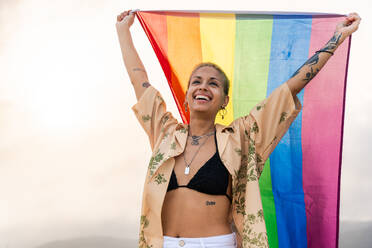 Beautiful lesbian woman holding LGBT flag at the beach, concepts about LGBTQ community, diversity, love and lifestyle - DMDF10345