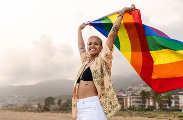 Beautiful lesbian woman holding LGBT flag at the beach, concepts about LGBTQ community, diversity, love and lifestyle - DMDF10347