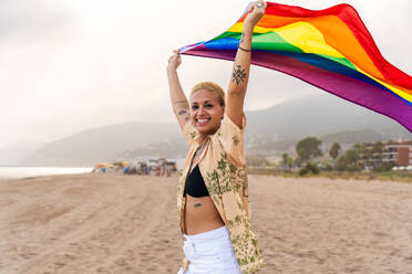Beautiful lesbian woman holding LGBT flag at the beach, concepts about LGBTQ community, diversity, love and lifestyle - DMDF10349