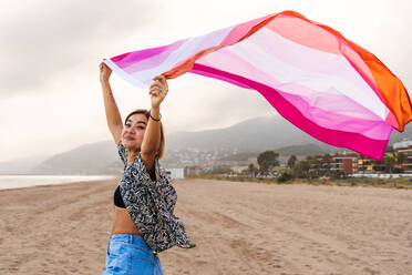 Beautiful lesbian woman holding LGBT flag at the beach, concepts about LGBTQ community, diversity, love and lifestyle - DMDF10354