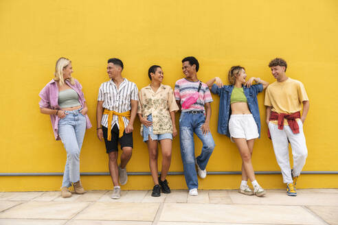 Unbeschwerte Freunde in farbenfroher Kleidung unterhalten sich vor einer gelben Wand - OIPF03921