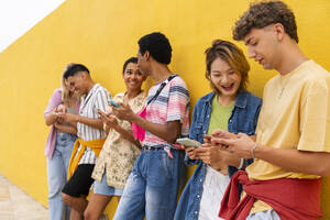 Gruppe von Freunden lehnt an einer gelben Wand und benutzt ihre Smartphones - OIPF03926